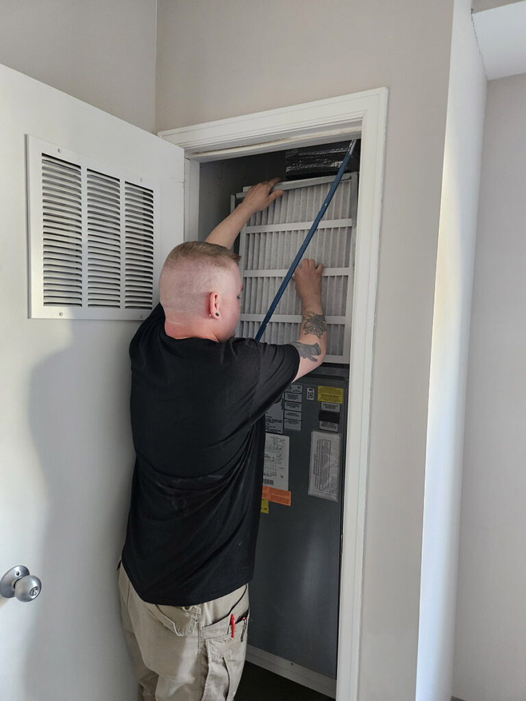 A man changing a furnace filter in a room, ensuring proper ventilation and maintenance.