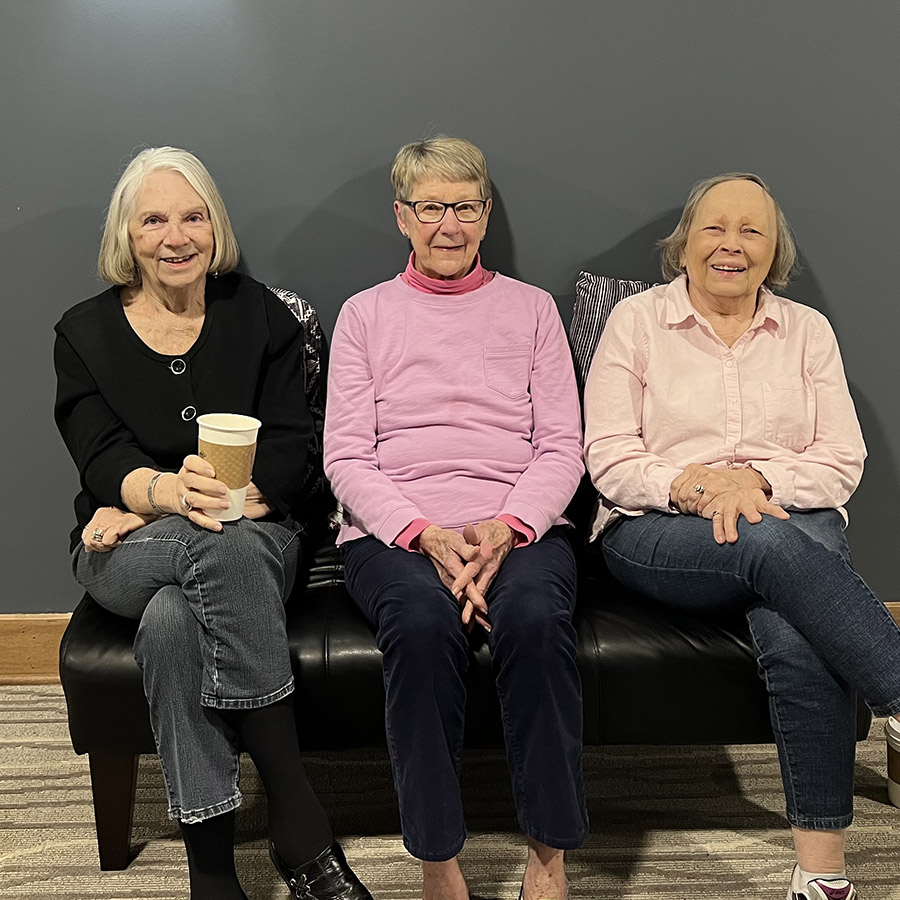 Three senior ladies chatting over coffee on a couch.