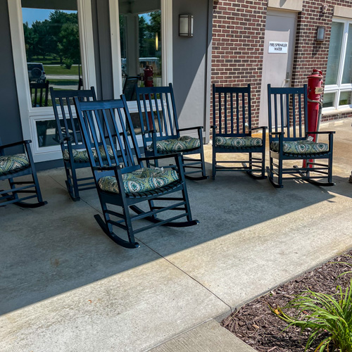 Black rocking chairs with patterned cushions arranged on a covered patio at Rock Creek Senior Living.