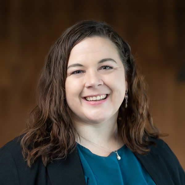 Karin Price, Resident Services Director at Rock Creek Senior Living, smiling warmly in a teal blouse and black blazer, with wavy brown hair against a softly lit background.
