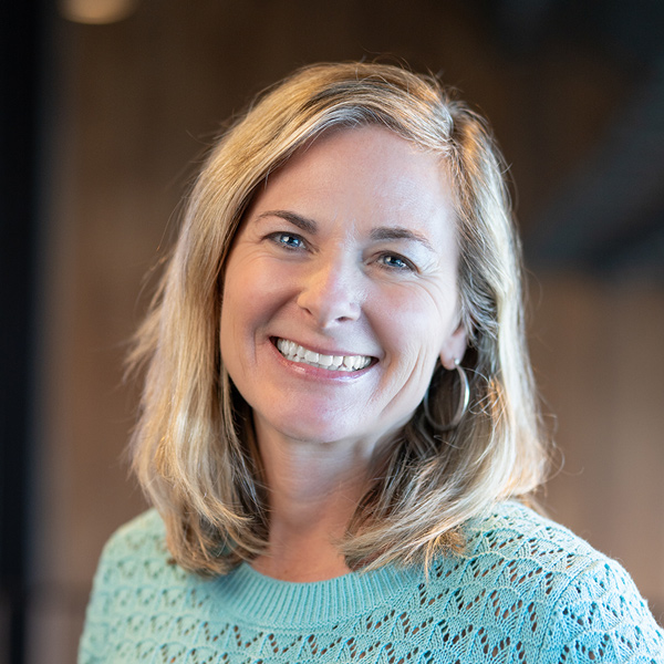 Tiffany Christensen, Senior Living Director at Rock Creek Senior Living, smiles warmly while wearing a mint green sweater, standing against a softly lit background.