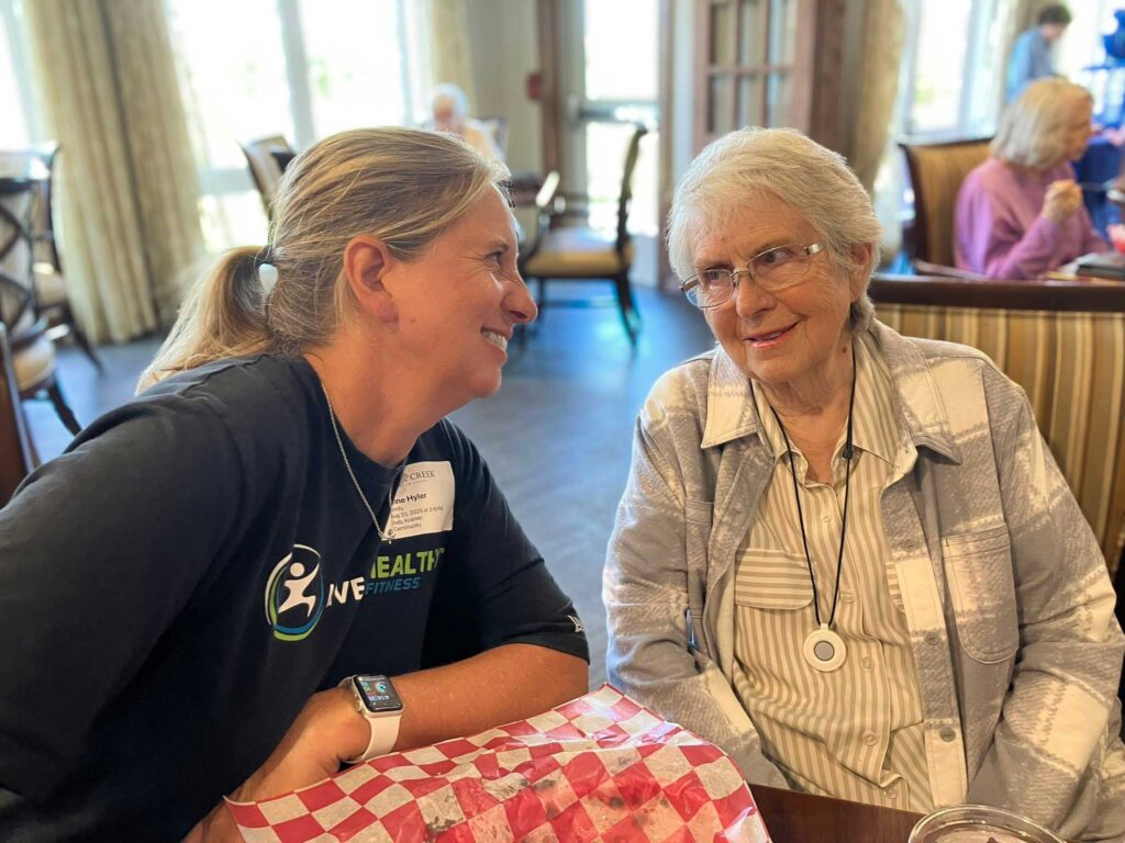Senior resident sharing a heartfelt conversation with a staff member at the community dining area, enjoying companionship and connection over lunch.