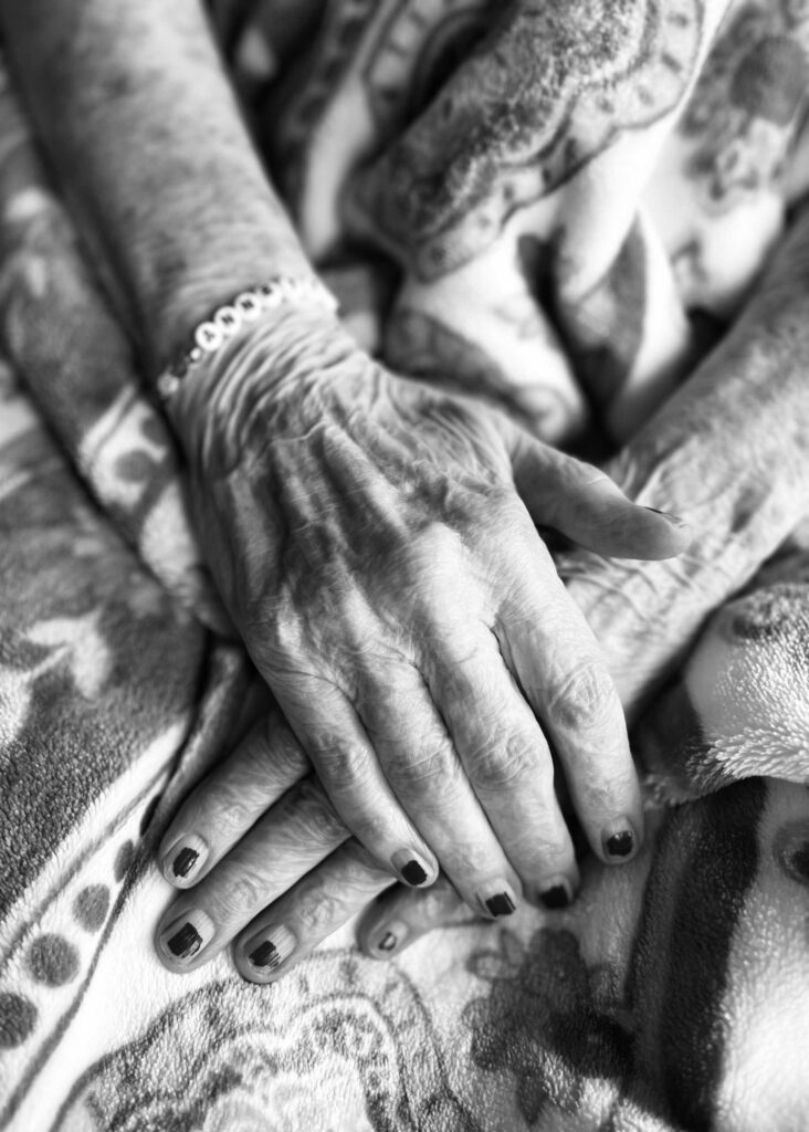 Black and white close-up of a senior resident’s hands resting on a patterned blanket, highlighting the beauty of age, life experience, and gentle moments of care.