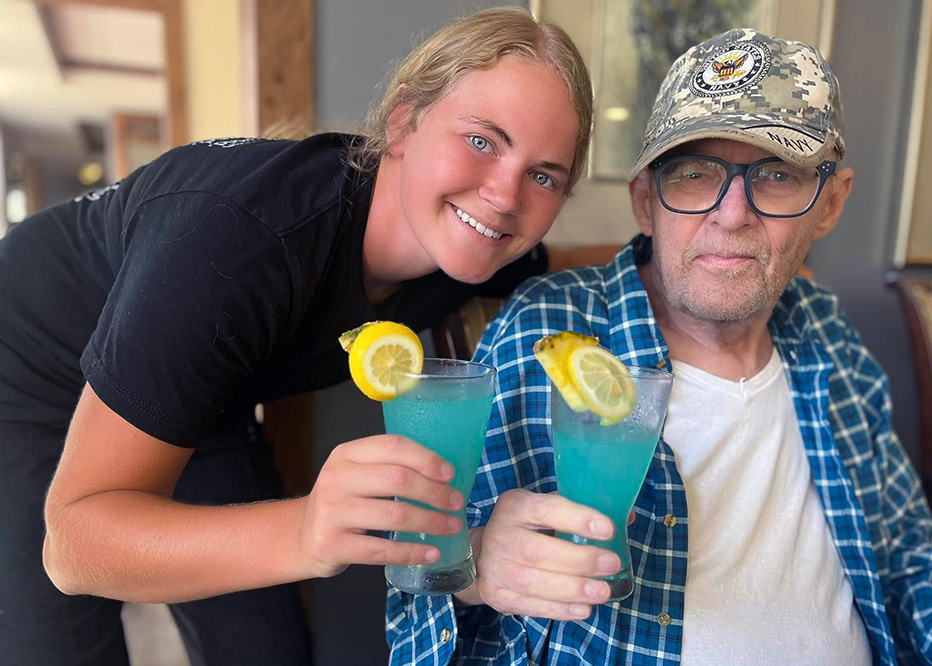 A team member and senior man hold glasses of blue drink with lemon slices.
