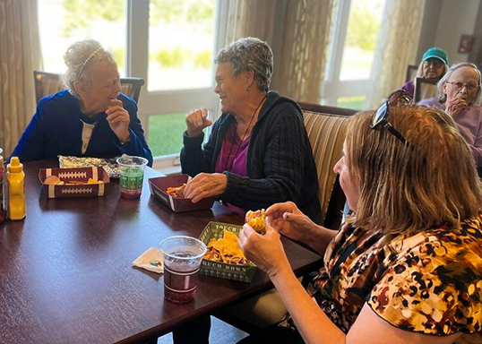 A group of senior friends laugh while enjoying a tailgate themed meal.
