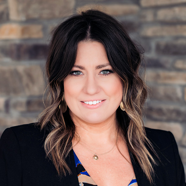 Crystal Swartzlander, Wellness Director at Rock Creek Senior Living, smiling in a professional headshot, wearing a black blazer, with shoulder-length dark hair and a softly blurred stone background.