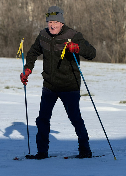 A senior man smiles while skiing on a snowy day.