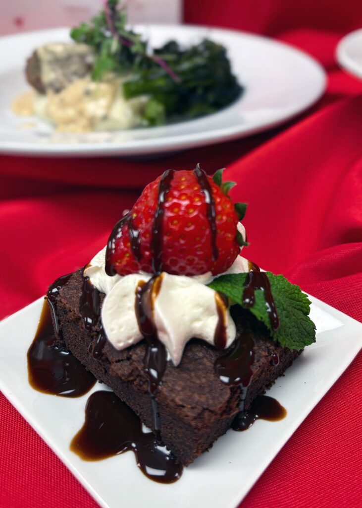 Valentines dinner dishes of chef-prepared brownie with chocolate drizzle, fresh whipped cream and strawberries, and a savory entry.