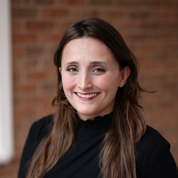 Hannah Dannewitz, Assistant Executive Director at Rock Creek Senior Living, smiling in a professional headshot, wearing a black top, standing in front of a softly blurred brick wall background.