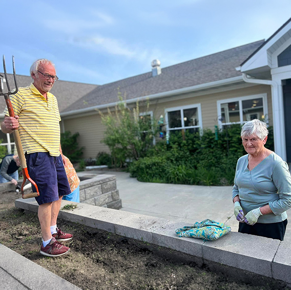 A senior man and woman ready their supplies to tend to a flower bed on a sunny day.