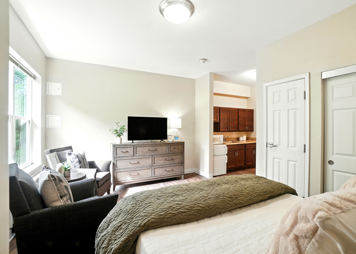 Bright senior living apartment at Rock Creek Senior Living featuring a bedroom, sitting area, kitchenette, and large window.