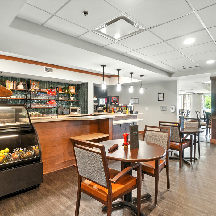 Senior living café and bistro area with beverage station, café seating, and snack display counter.