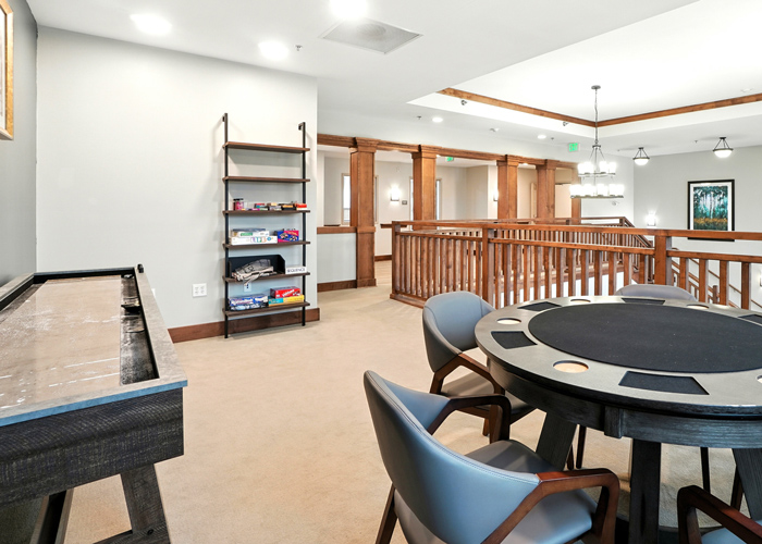 Senior living game room with card table, shuffleboard, comfortable seating, and open community gathering space.