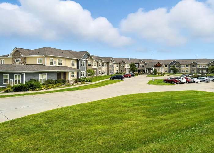 Wide exterior view of a senior living community with landscaped grounds, walking paths, and resident parking areas.